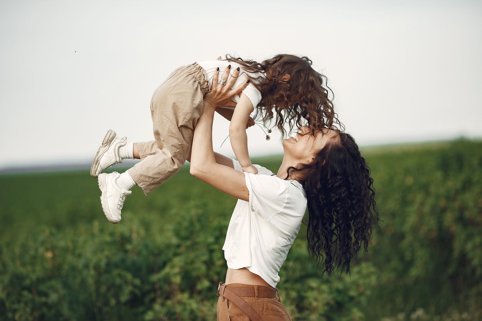 A parent lifting a laughing child into the air in a sunlit field