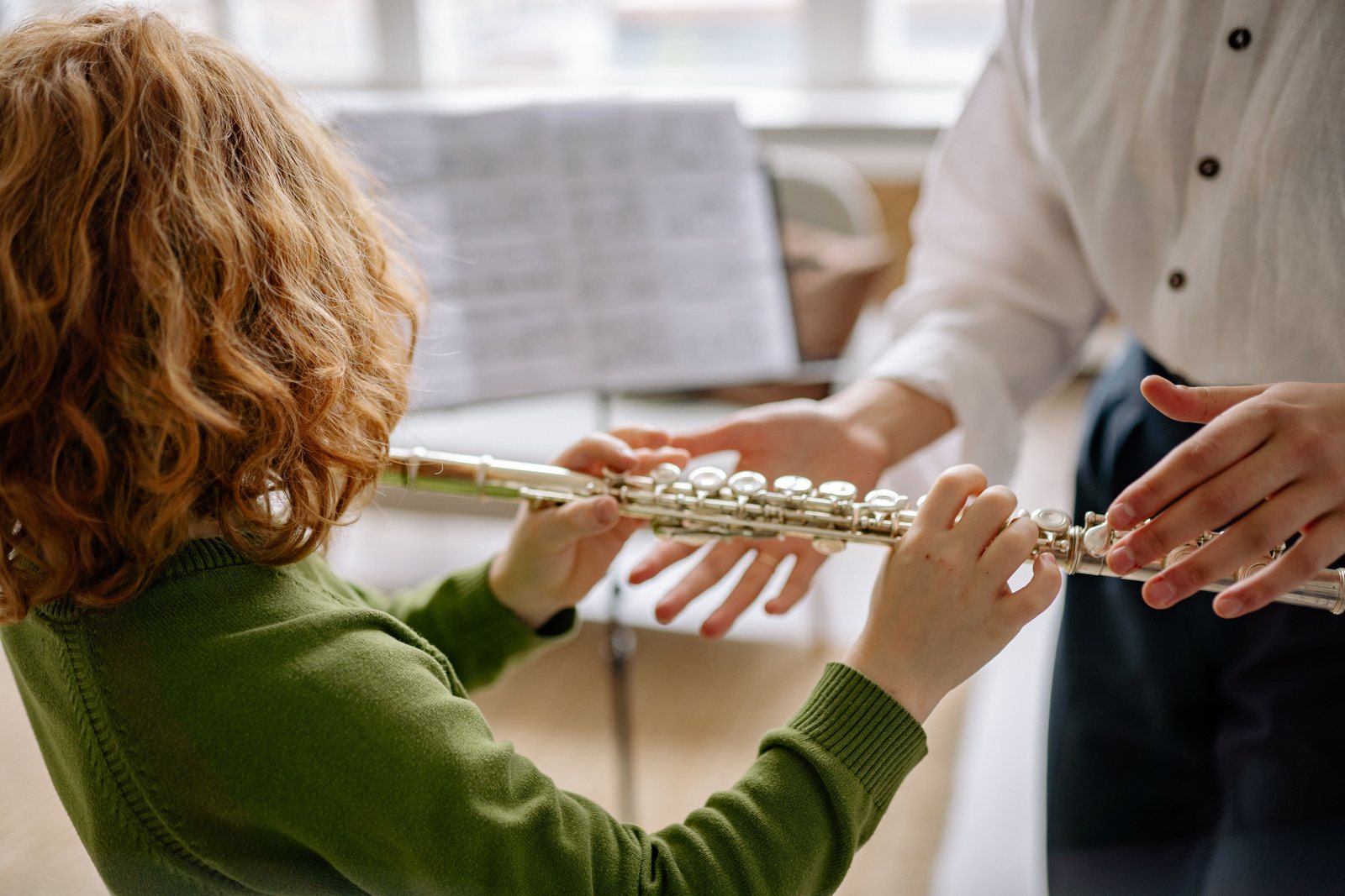 A teacher guiding a child's hands on a flute